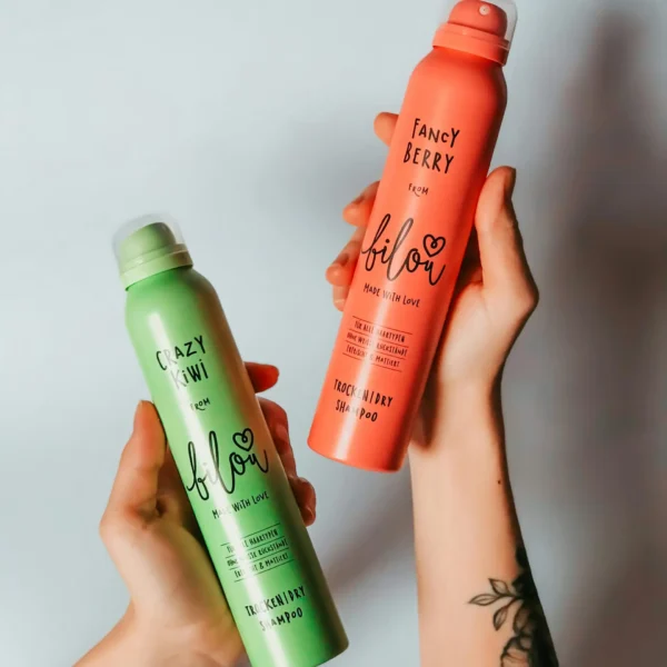 Close-up of hands holding vibrant kiwi and berry scented deodorant cans against a neutral background.