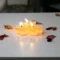 Cozy scene of lit candles surrounded by fall leaves on a white table, indoors.